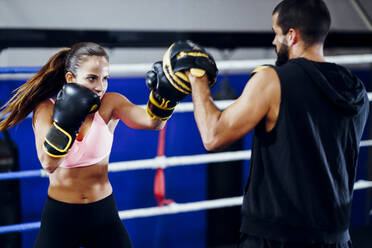 Weibliche Boxerin beim Sparring mit ihrem Trainer im Fitnessstudio - JSMF01536