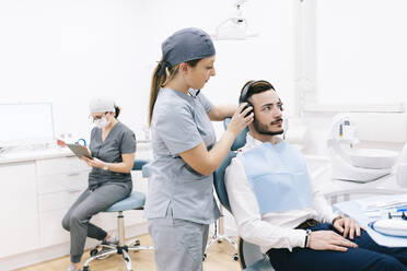 Medical secretary preparing dental treatment putting on headphones on patient's head - DGOF00604