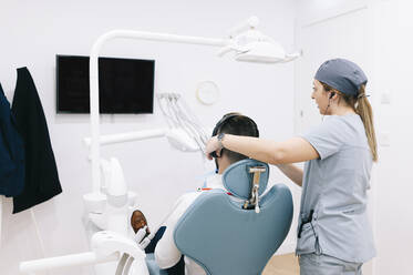 Medical secretary preparing dental treatment putting on headphones on patient's head - DGOF00605