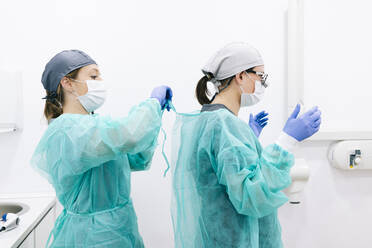 Two dentists putting on sterile protective clothing - DGOF00622