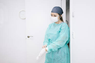 Dentist wearing protective suit putting on gloves - DGOF00626