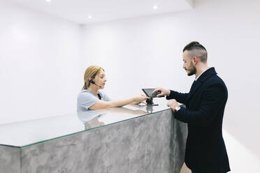 Young man at reception desk of a medical practice using digital device - DGOF00635