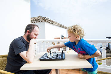 Vater und Sohn spielen Schach auf einer Dachterrasse, Spanien - IHF00317