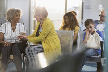 Ärztin untersucht die Hand eines älteren Patienten im Rollstuhl in der Kliniklobby - CAIF24909