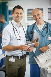 Porträt eines selbstbewussten männlichen Arztes, der ein digitales Tablet im Krankenhaus benutzt - CAIF24911