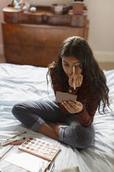 Teenage girl applying eyeshadow makeup on bed - CAIF24915