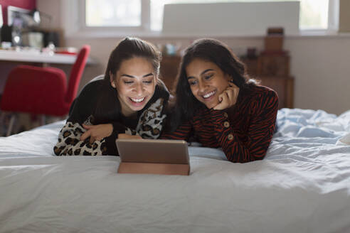 Glückliche Mädchen im Teenageralter benutzen ein digitales Tablet auf dem Bett - CAIF24918