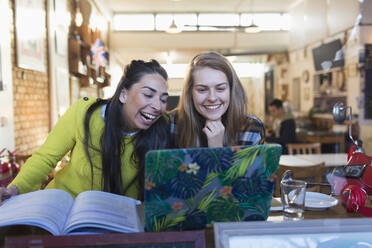 Fröhliche, lachende junge Studentinnen mit Laptop in einem Caféfenster - CAIF24929