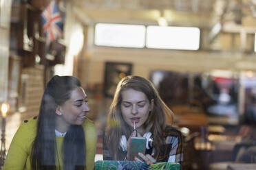 Junge Frauen tragen Lipgloss im Schaufenster eines Cafés auf - CAIF24935