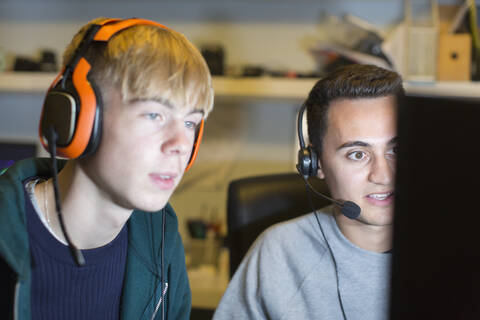 Teenager mit Kopfhörern spielen ein Videospiel am Computer, lizenzfreies Stockfoto