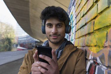 Porträt eines selbstbewussten jungen Mannes, der mit Kopfhörern und mp3-Player Musik hört - CAIF24976