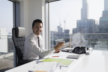 Porträt eines selbstbewussten Geschäftsmannes, der ein Smartphone in einem Hochhausbüro benutzt - CAIF24987