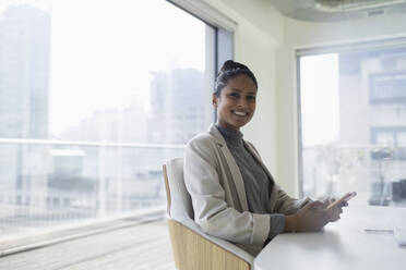 Portrait happy, confident businesswoman with smart phone in conference room - CAIF24996