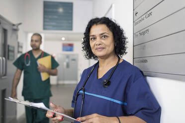 Porträt einer selbstbewussten Ärztin mit Krankenblatt bei der Visite im Krankenhausflur - CAIF25029