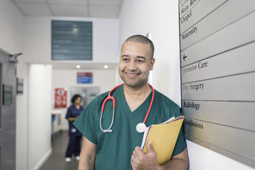 Porträt eines lächelnden, selbstbewussten männlichen Chirurgen im Krankenhausflur - CAIF25031
