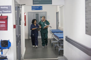 Arzt und Chirurg besprechen Krankenakte, gehen im Krankenhauskorridor spazieren - CAIF25039