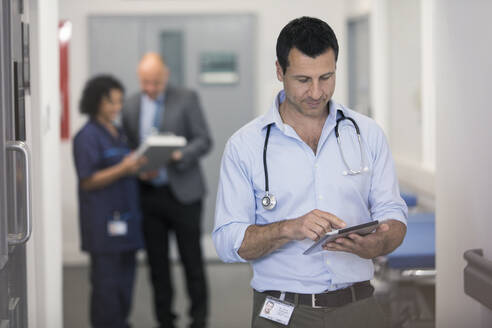 Männlicher Arzt mit digitalem Tablet im Krankenhausflur - CAIF25040