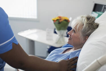 Caring female nurse comforting senior woman resting in hospital bed - CAIF25048