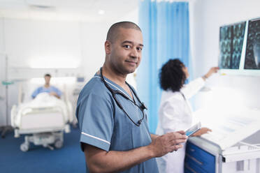 Portrait confident, smiling doctor using digital tablet in hospital room - CAIF25071