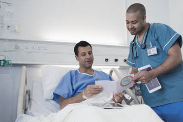 Männlicher Patient zeigt einer Krankenschwester im Krankenhauszimmer eine Grußkarte - CAIF25073