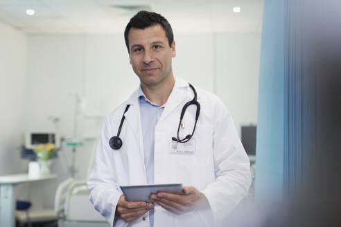 Porträt selbstbewusster männlicher Arzt, der ein digitales Tablet in einem Krankenhauszimmer benutzt - CAIF25074