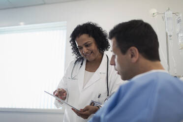 Doctor with digital tablet making rounds, talking with patient in hospital room - CAIF25075