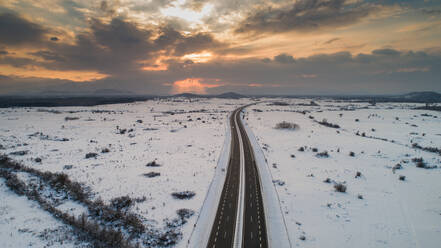 Luftaufnahme des winterlichen Sonnenuntergangs und des Schnees auf der A1, der Hauptautobahn in Kroatien, die die Städte Split und Zagreb verbindet, aufgenommen in Lika. - AAEF07453