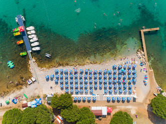 Luftaufnahme von oben der blauen Sonnenschirme am Strand von Medulin im Sommer, Kroatien. - AAEF07693