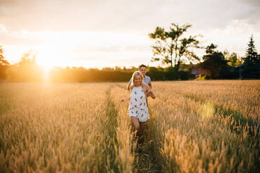 Lächelndes junges Paar geht bei Sonnenuntergang durch ein goldenes Weizenfeld. - ISF23978