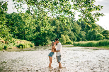 Young couple standing ankle deep in a river, hugging and kissing. - ISF23995