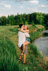 Ein junges Paar steht auf einem Weg an einem Fluss, umarmt und küsst sich. - ISF24000