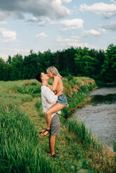 Ein junges Paar steht auf einem Weg an einem Fluss, umarmt und küsst sich. - ISF24001