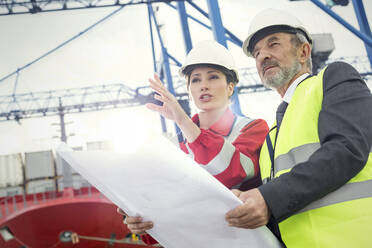 Dockarbeiter und Manager mit Blaupause im Gespräch auf der Werft - CAIF25085