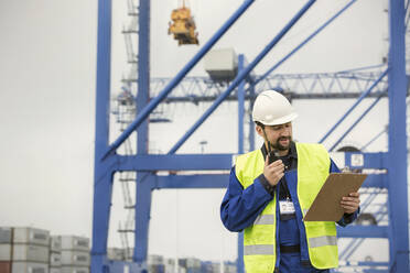 Dock worker with walkie-talkie and clipboard at shipyard - CAIF25086