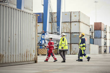 Dockarbeiter gehen entlang von Frachtcontainern auf einer Werft - CAIF25095