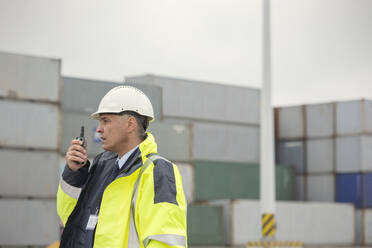 Dockmanager mit Walkie-Talkie zwischen Frachtcontainern auf einer Werft - CAIF25100