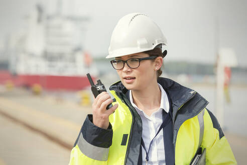 Weiblicher Hafenarbeiter mit Walkie-Talkie in einer Werft - CAIF25107