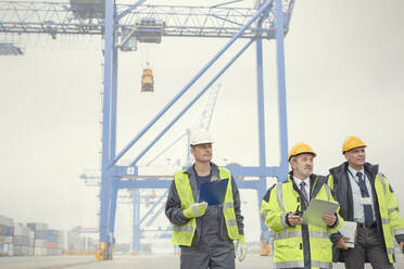 Dock workers and manager walking below crane at shipyard - CAIF25123