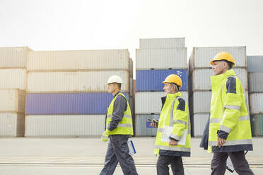 Dockarbeiter gehen entlang von Frachtcontainern auf einer Werft - CAIF25125