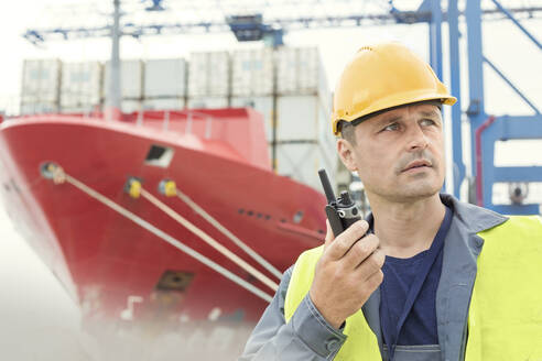 Dock worker using walkie-talkie below container ship at shipyard - CAIF25128
