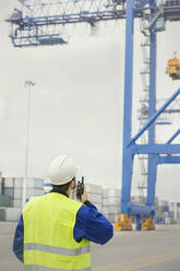 Hafenarbeiter mit Walkie-Talkie, der einen Kran auf einer Werft beobachtet - CAIF25138