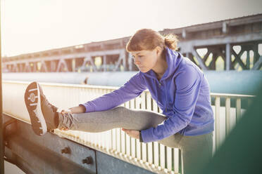 Young female runner stretching leg on urban railing - CAIF25145