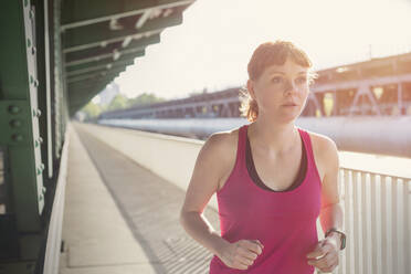 Determined young woman running along sunny train station platform - CAIF25147