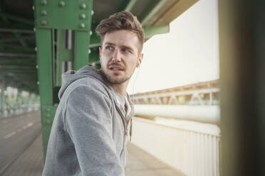 Young male runner with headphones looking over shoulder on train station platform - CAIF25149