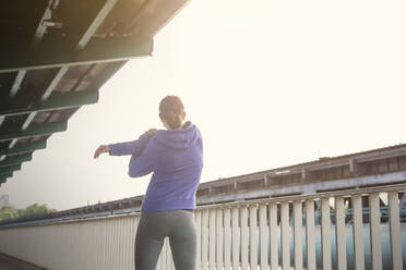 Junge Läuferin streckt die Arme entlang eines städtischen Geländers - CAIF25156