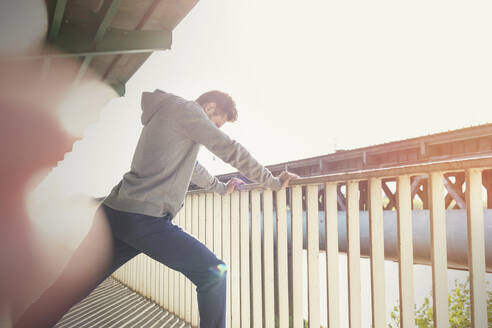 Junger männlicher Läufer, der sein Bein an einem sonnigen städtischen Geländer ausstreckt - CAIF25169