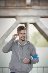 Porträt selbstbewusster junger männlicher Läufer mit Kopfhörern und mp3-Player-Armband - CAIF25178