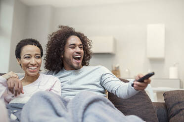Glückliches Paar, das sich auf dem Wohnzimmersofa entspannt und fernsieht - CAIF25182