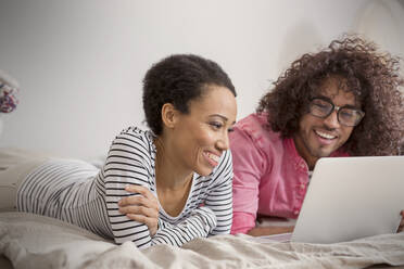 Lächelndes Paar mit Laptop auf dem Bett - CAIF25198