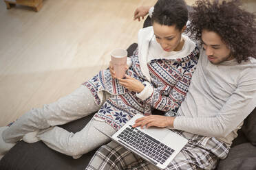 Affectionate couple in pajamas relaxing, using laptop on sofa - CAIF25206